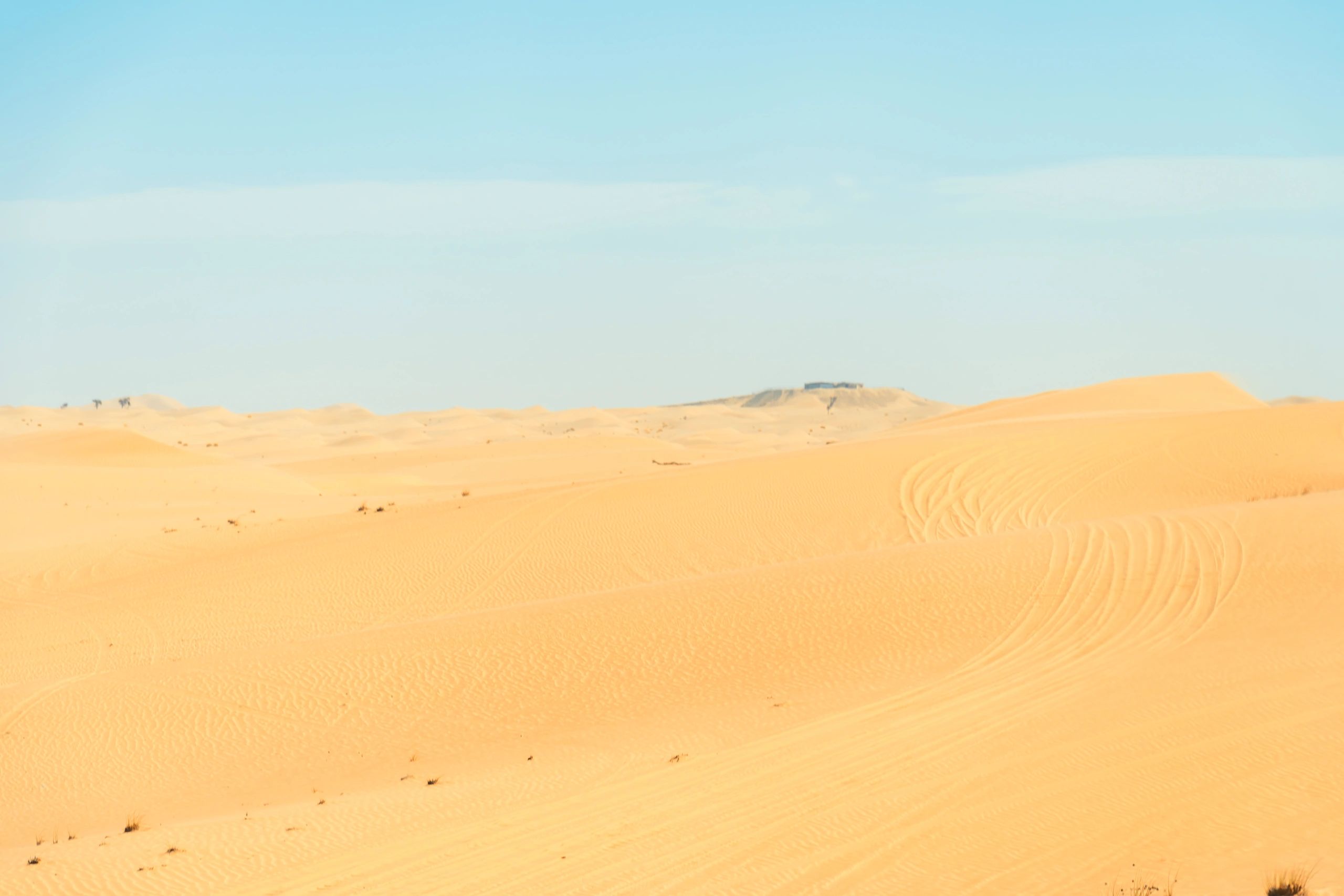 A wide shot of a sandy desert landscape under a clear blue sky